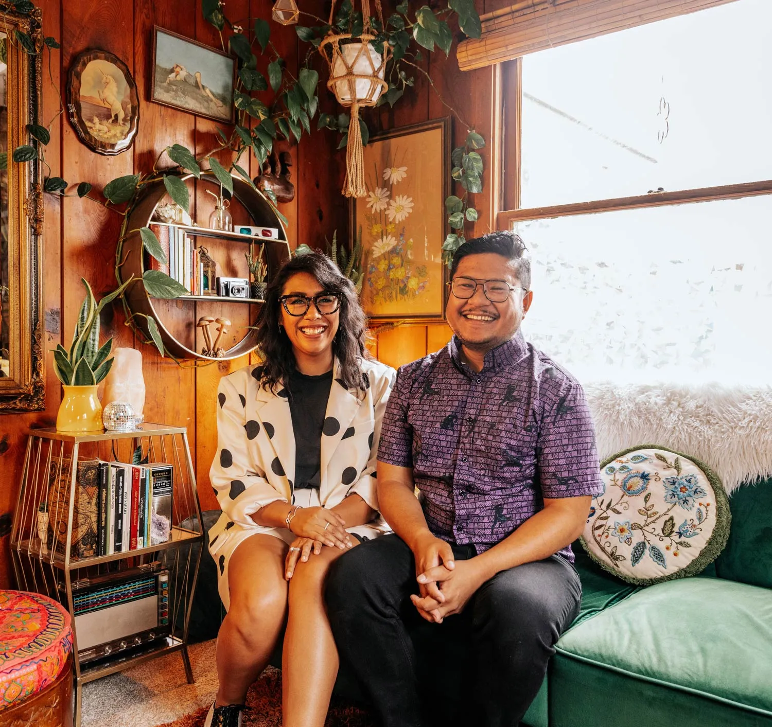 Jess and Nelson smiling together on the green couch in the studio